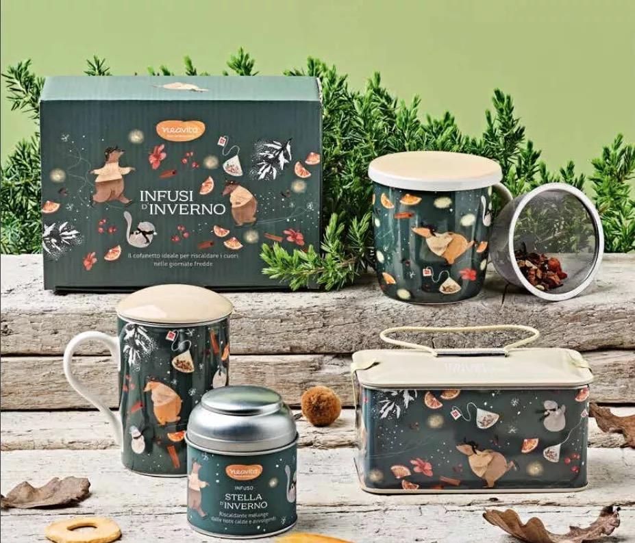 The Infusi d’inverno line: illustrated dark green box, mugs, tin and the Stella d’inverno jar, on wood among pine branches