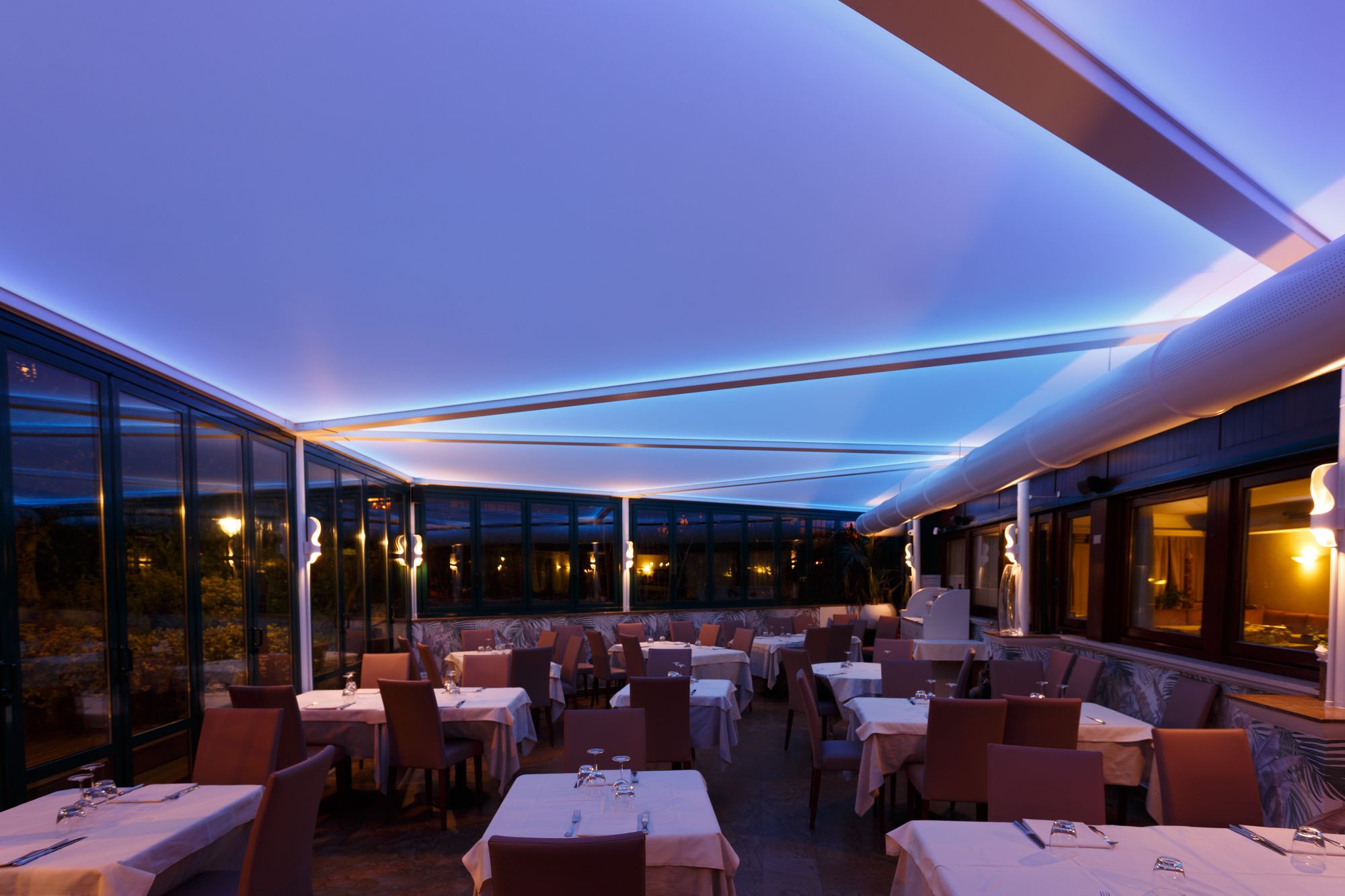 A restaurant dining room in the evening with a Savi ceiling spreading a soft blue light